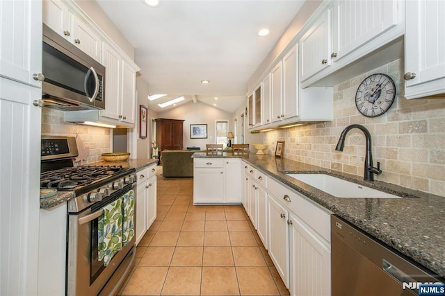 kitchen with light tile patterned floors, a sink, stainless steel appliances, vaulted ceiling, and white cabinetry