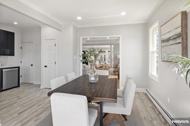 dining room featuring a baseboard heating unit, baseboards, crown molding, and light wood finished floors