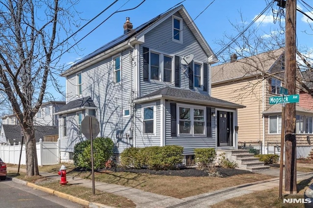 view of front of home with fence, roof mounted solar panels, and a chimney