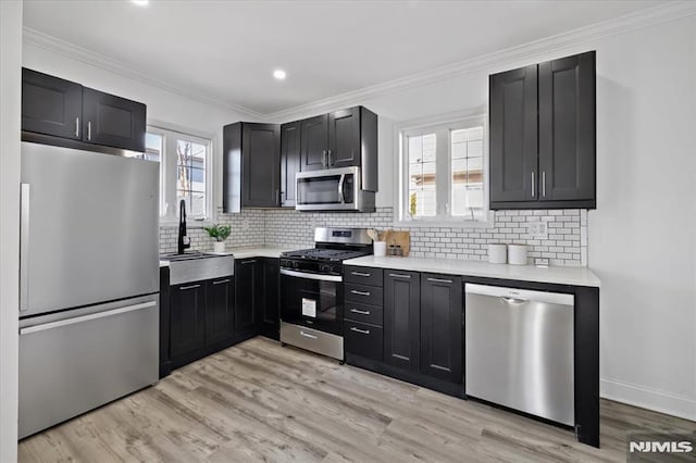 kitchen featuring light wood finished floors, light countertops, ornamental molding, stainless steel appliances, and a sink