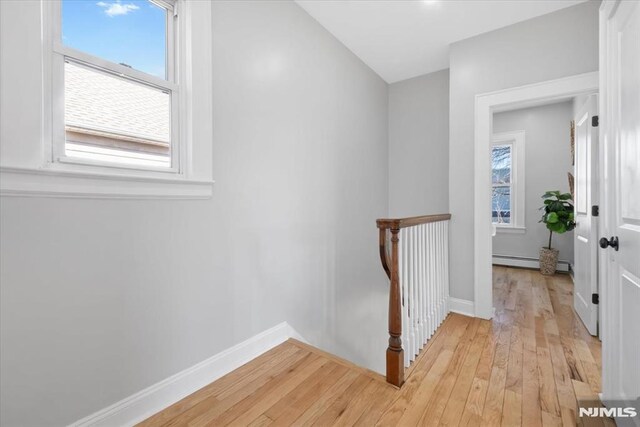 corridor with an upstairs landing, light wood-style flooring, baseboards, and a baseboard radiator