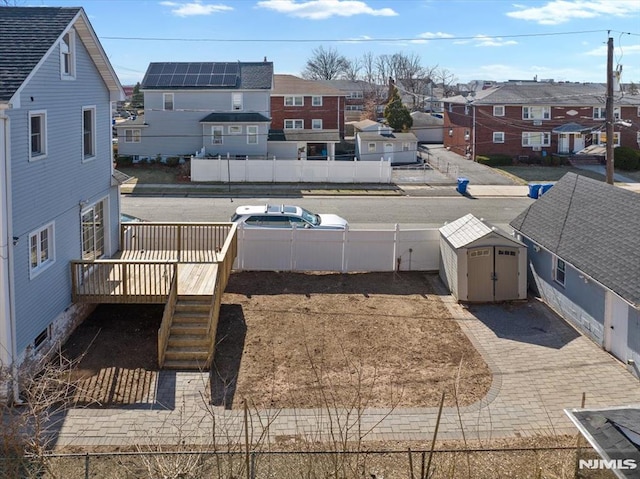 view of yard with a residential view, a storage shed, a fenced backyard, a deck, and an outbuilding