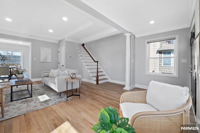 living room with baseboards, light wood finished floors, decorative columns, ornamental molding, and stairs