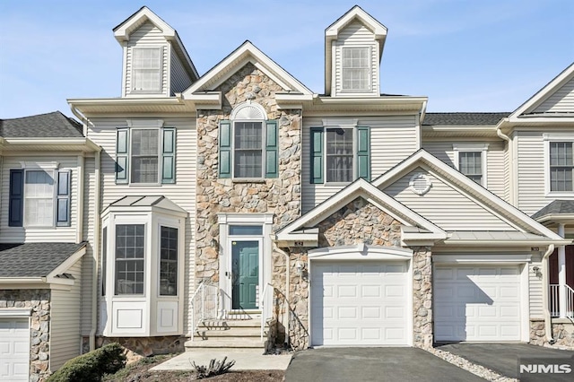 view of property with aphalt driveway, stone siding, and an attached garage