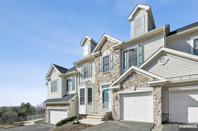 townhome / multi-family property featuring stone siding, an attached garage, and driveway