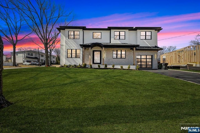 view of front of house featuring a yard, stone siding, an attached garage, and driveway