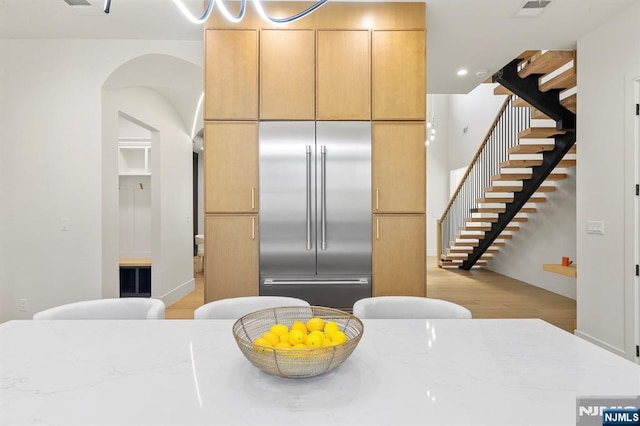 kitchen featuring visible vents, built in fridge, recessed lighting, arched walkways, and light stone countertops