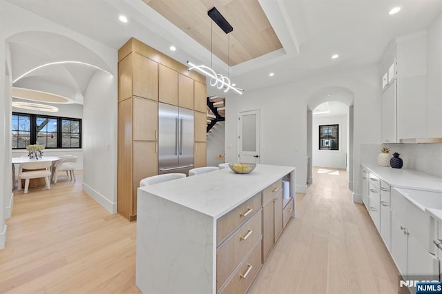 kitchen with arched walkways, a raised ceiling, modern cabinets, and a center island