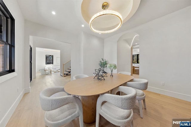 dining room with arched walkways, recessed lighting, baseboards, and light wood-style floors