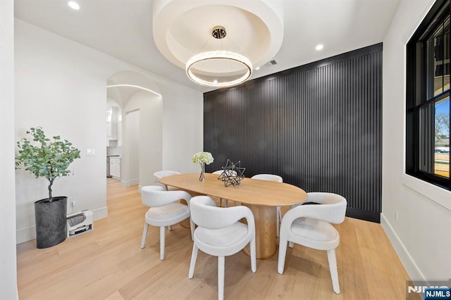 dining space with arched walkways, recessed lighting, light wood-style flooring, and baseboards