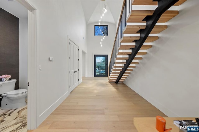 hall featuring light wood finished floors, stairs, baseboards, and a towering ceiling