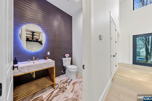 half bath featuring vanity, toilet, baseboards, and a wealth of natural light