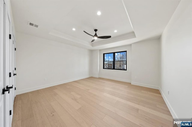 unfurnished room with a tray ceiling, visible vents, light wood-style floors, and a ceiling fan