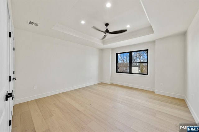 unfurnished room featuring a raised ceiling, light wood-style floors, visible vents, and ceiling fan