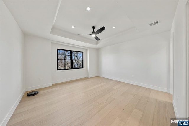 spare room featuring a raised ceiling, baseboards, light wood finished floors, and ceiling fan