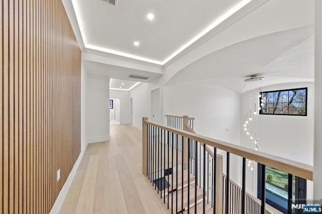 hallway featuring light wood-style floors, an upstairs landing, visible vents, and a wealth of natural light