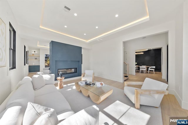 living room with visible vents, light wood-style flooring, a large fireplace, and a tray ceiling