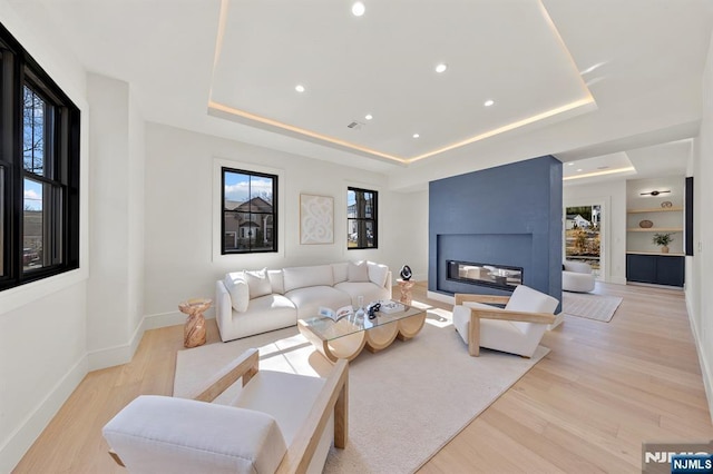 living room featuring built in shelves, a raised ceiling, baseboards, and wood finished floors