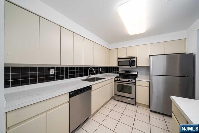 kitchen featuring a sink, tasteful backsplash, cream cabinets, stainless steel appliances, and light countertops