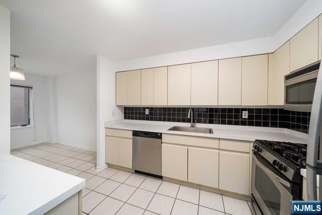 kitchen featuring cream cabinetry, stainless steel appliances, light countertops, and a sink