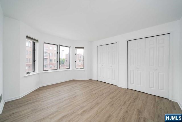 unfurnished bedroom with wood finished floors, baseboards, and two closets