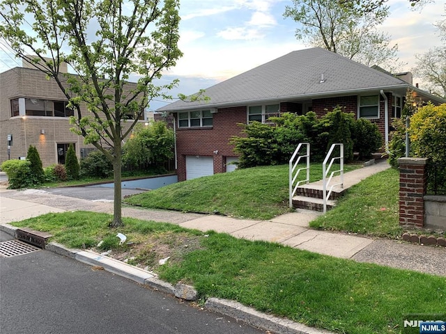 single story home featuring brick siding, a front yard, roof with shingles, a garage, and driveway