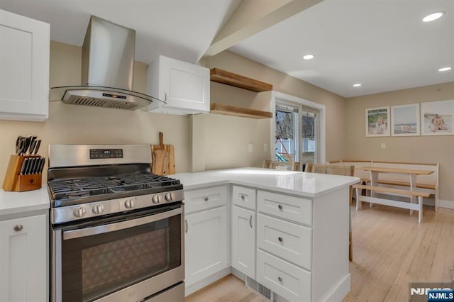 kitchen with a peninsula, open shelves, stainless steel range with gas stovetop, white cabinets, and wall chimney range hood