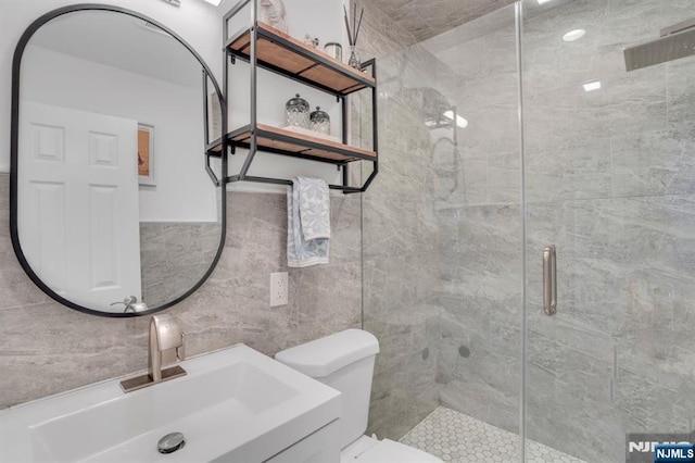 bathroom with vanity, a shower stall, toilet, and tile walls