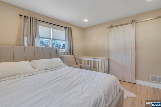 bedroom with visible vents, baseboards, a barn door, recessed lighting, and hardwood / wood-style flooring