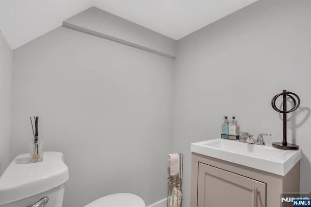 bathroom featuring toilet, vanity, and vaulted ceiling