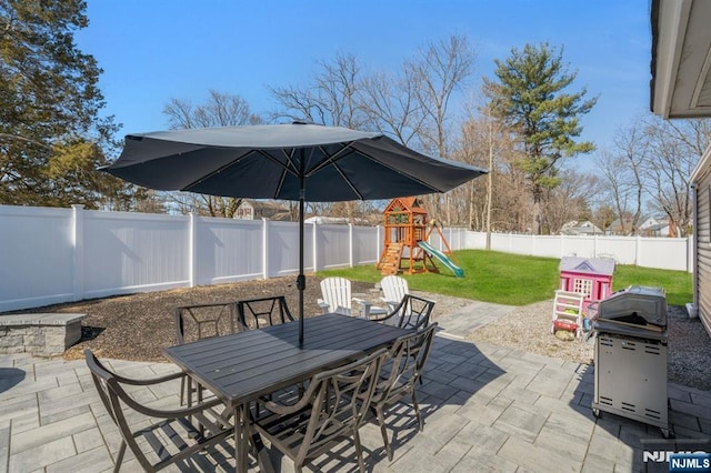 view of patio with outdoor dining space, a playground, and a fenced backyard