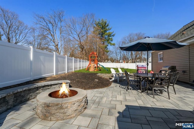 view of patio with outdoor dining space, a playground, a fenced backyard, and a fire pit