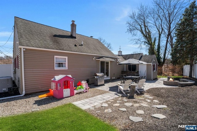 rear view of house with a patio, fence, roof with shingles, and an outdoor fire pit