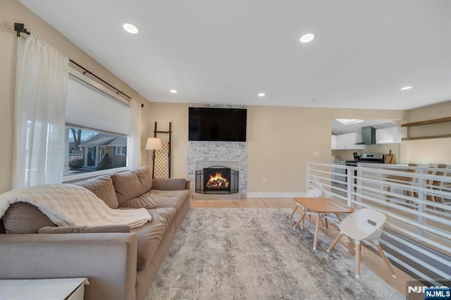 living room featuring light wood finished floors, a stone fireplace, recessed lighting, and baseboards