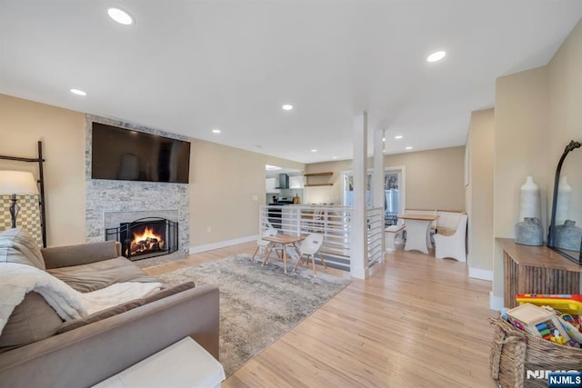 living area with recessed lighting, light wood-type flooring, and a stone fireplace