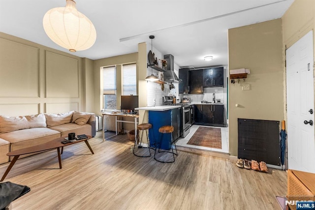 kitchen featuring stainless steel range with gas cooktop, light wood-style flooring, a sink, light countertops, and wall chimney exhaust hood