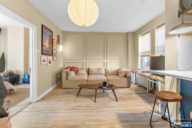 living area featuring light wood-type flooring, baseboards, and a decorative wall