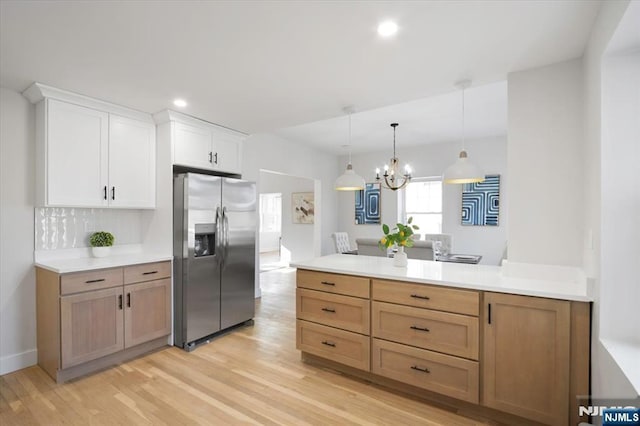 kitchen featuring a peninsula, light countertops, light wood-style floors, pendant lighting, and stainless steel fridge