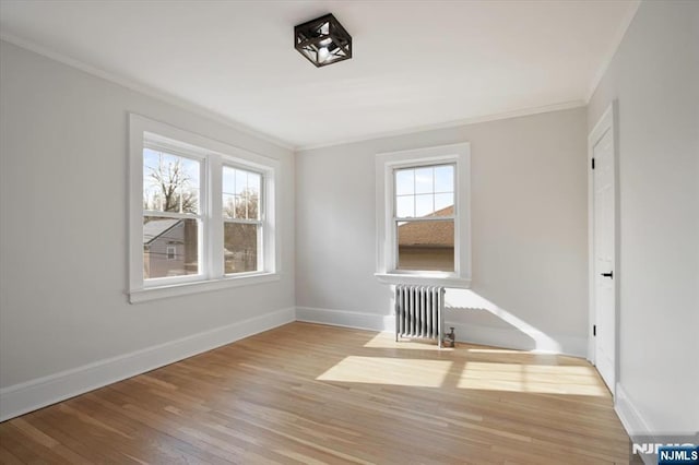 empty room with radiator heating unit, wood finished floors, baseboards, and ornamental molding