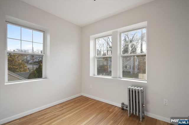 spare room with hardwood / wood-style flooring, radiator, baseboards, and a wealth of natural light