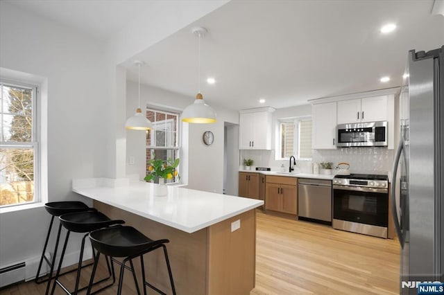 kitchen with a peninsula, a sink, stainless steel appliances, a kitchen breakfast bar, and backsplash