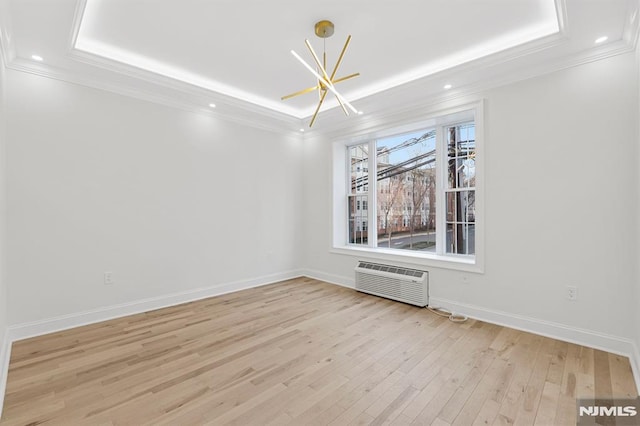 unfurnished room featuring ornamental molding, a wall mounted AC, a tray ceiling, light wood-style floors, and baseboards