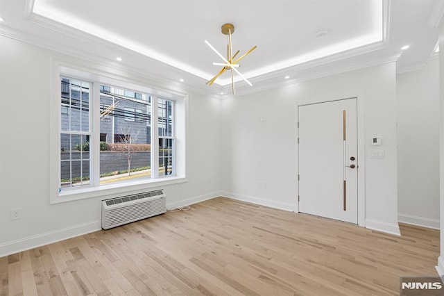 spare room featuring a wall mounted AC, an inviting chandelier, a tray ceiling, light wood-style floors, and crown molding