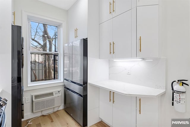 kitchen featuring light stone counters, white cabinetry, an AC wall unit, and freestanding refrigerator