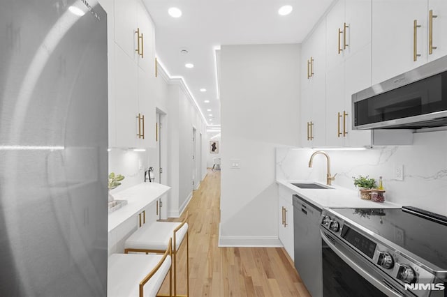kitchen with a sink, white cabinets, light wood-style floors, appliances with stainless steel finishes, and tasteful backsplash