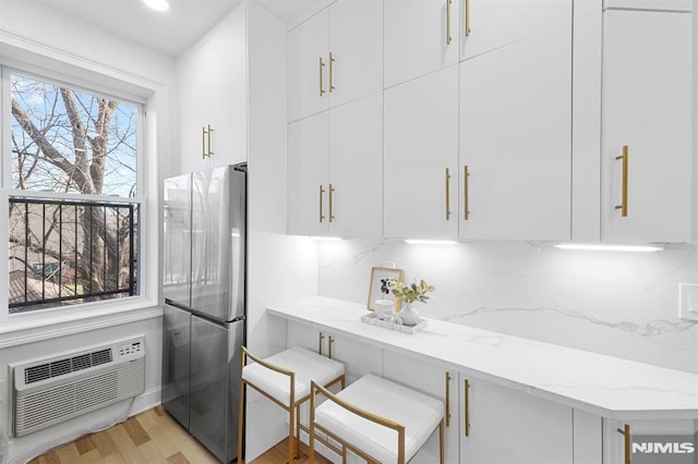 interior space featuring decorative backsplash, a wall mounted air conditioner, light stone countertops, and freestanding refrigerator