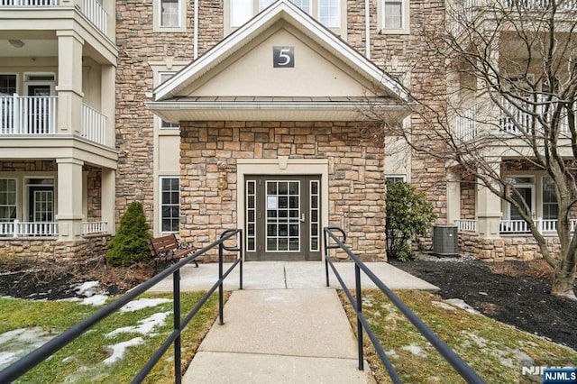 view of exterior entry featuring stone siding, stucco siding, and central AC