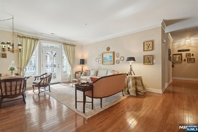 living area featuring hardwood / wood-style floors, crown molding, baseboards, and an inviting chandelier