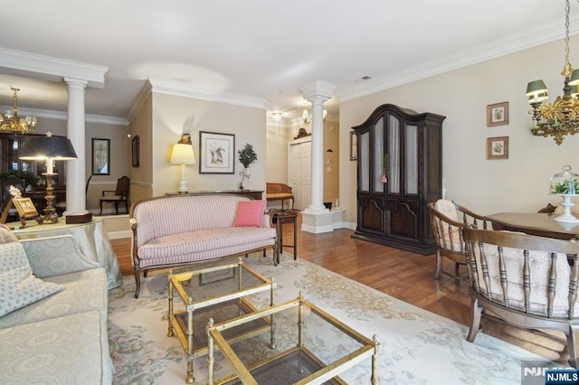 living room with wood finished floors, an inviting chandelier, crown molding, decorative columns, and baseboards