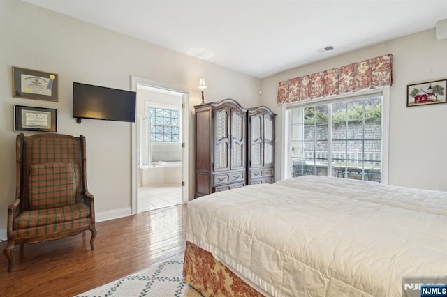 bedroom with visible vents, multiple windows, ensuite bathroom, and wood finished floors